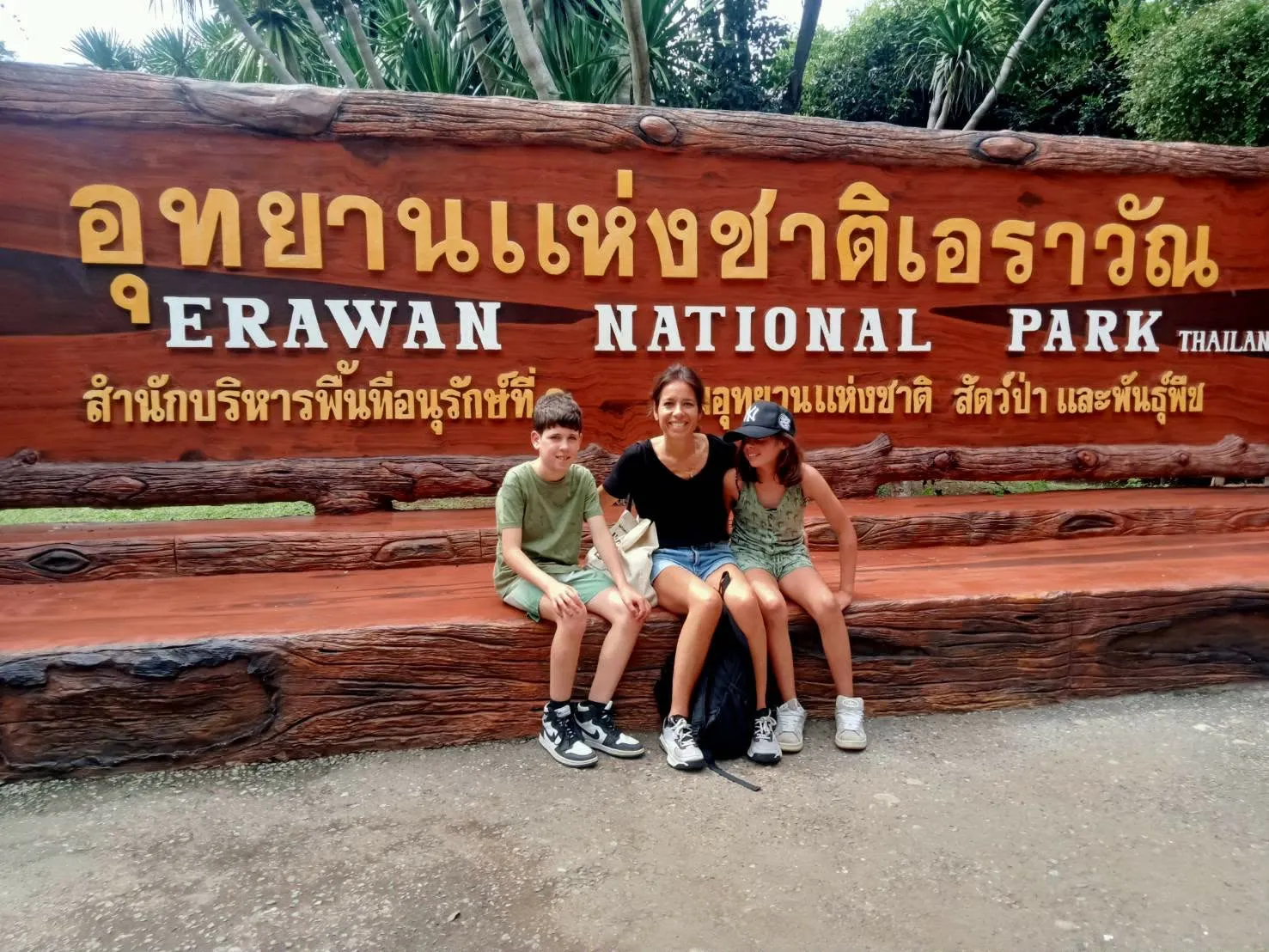 A mother and two children on the bench at the Erawan National Park sign