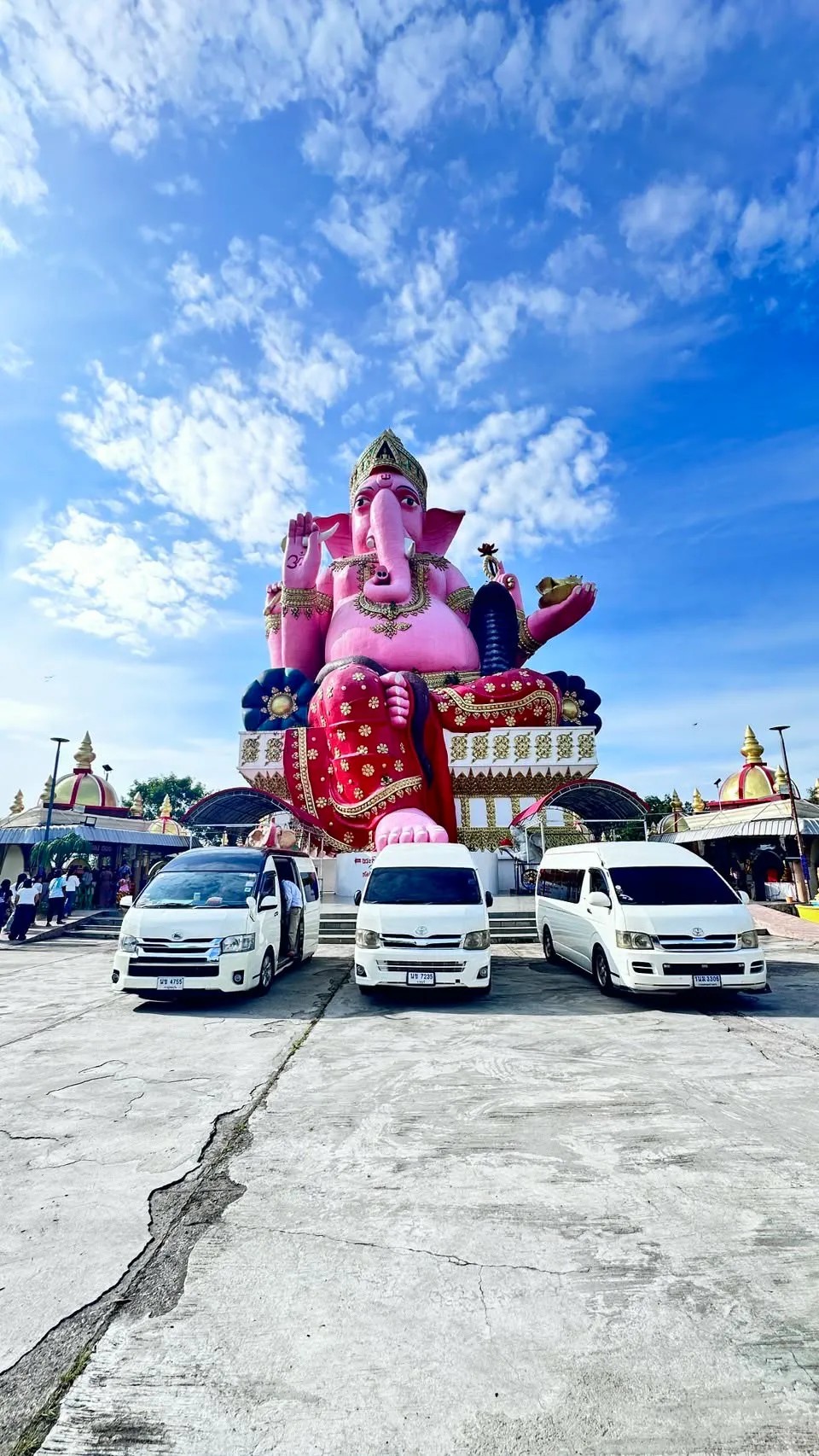 Three white vans parked in front of the giant pink Ganesha statue